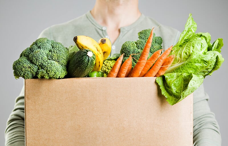 Person holding a box filled of veggies
