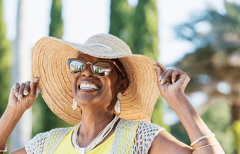 A woman outside smiling and touching the brim of her sun hat
