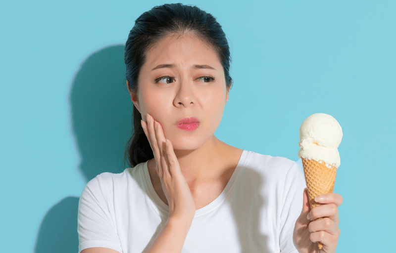 A woman holding her jaw and eyeing an ice cream cone