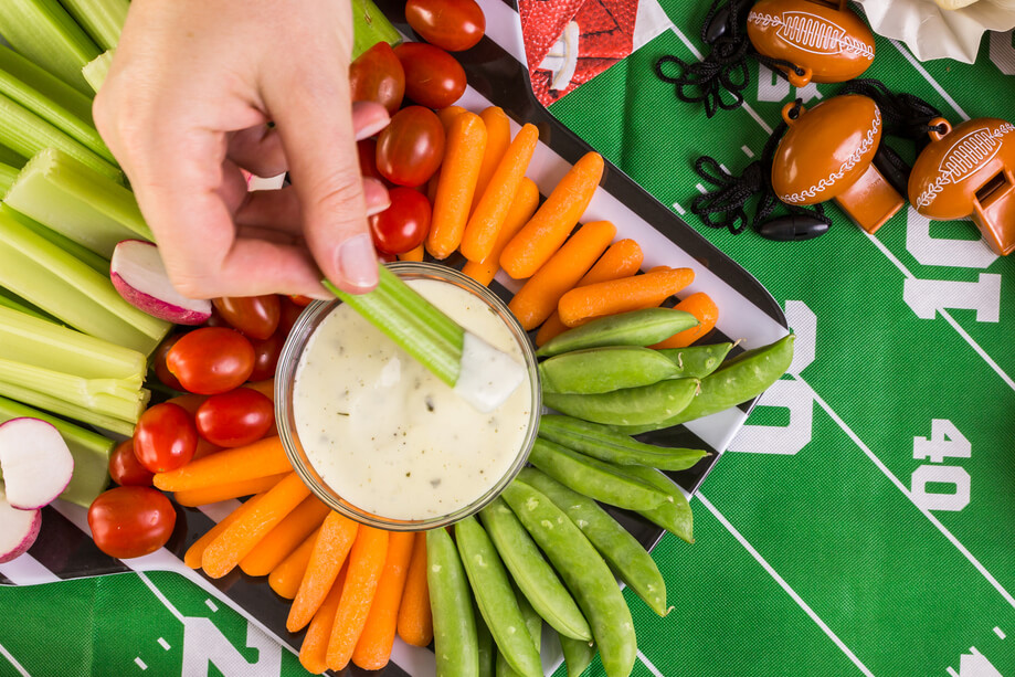 A hand dipping celery in dip