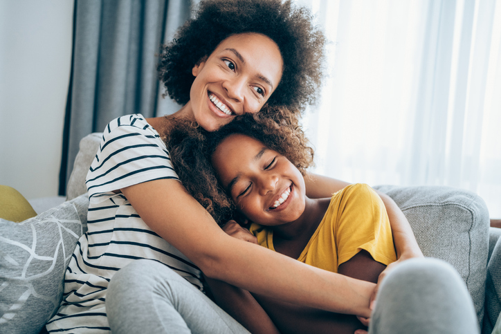 Lovely mother embracing her cute daughter on the sofa at home.