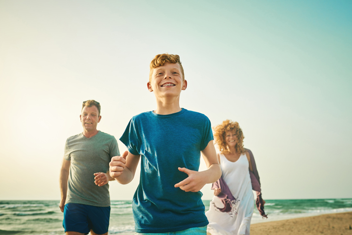 Shot of an adorable little boy running along the beach with his family