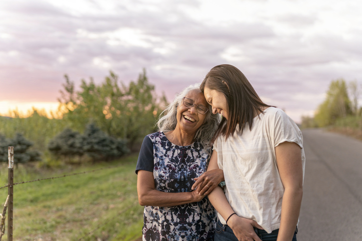 A beautiful senior mom of pacific island descent is walking outdoors with her adult thirty something year old daughter. They are enjoying each others company and soaking in the gorgeous, colorful, sunset.