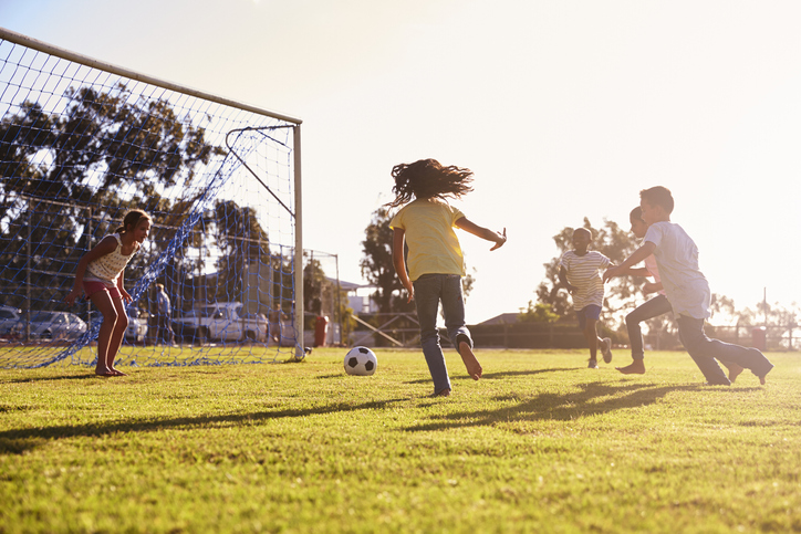 Girl defending goal at football game with family and friends