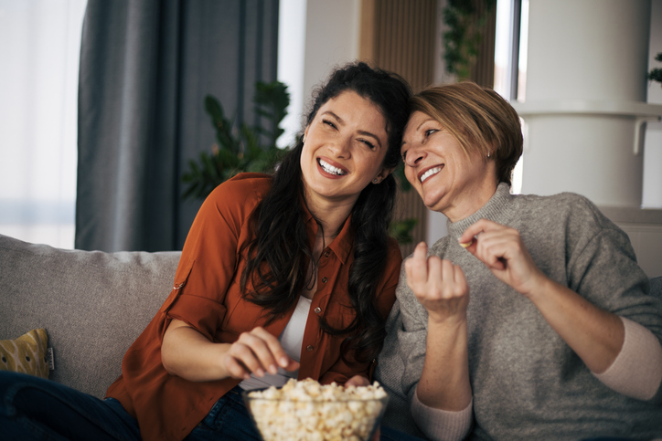 Mother and daughter watching movie together and eating pop corns while sitting on sofa.