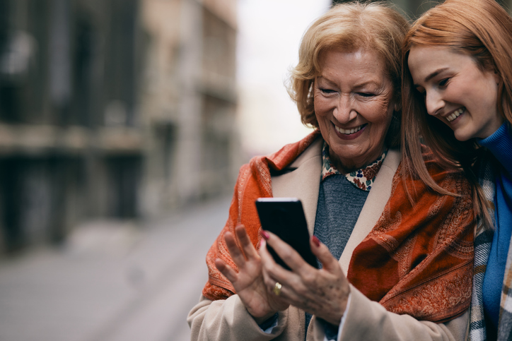 A grandmother and her grandchild standing on the street and reading messages on the phone.