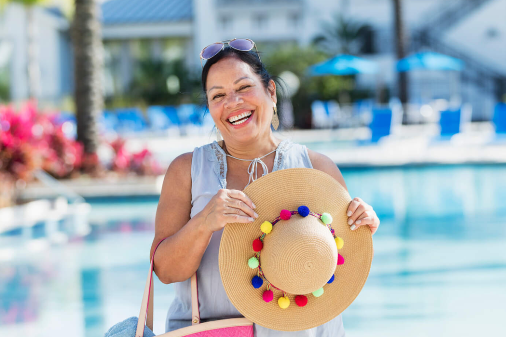 A woman at a pool holding her hat and smiling