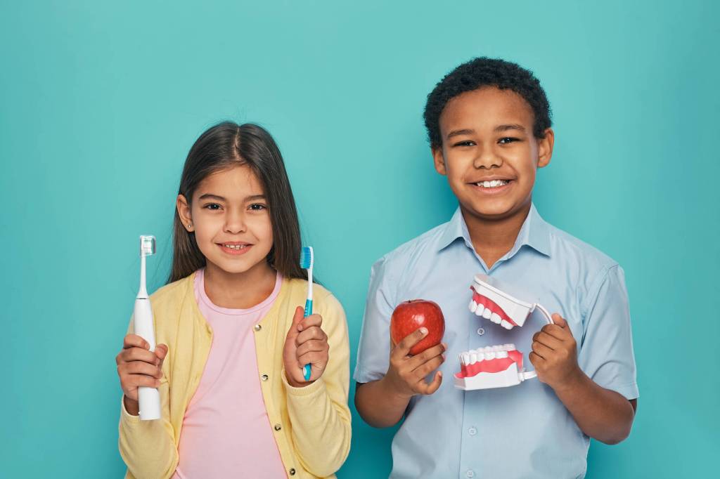 kids smiling with toothbrushes and an apple