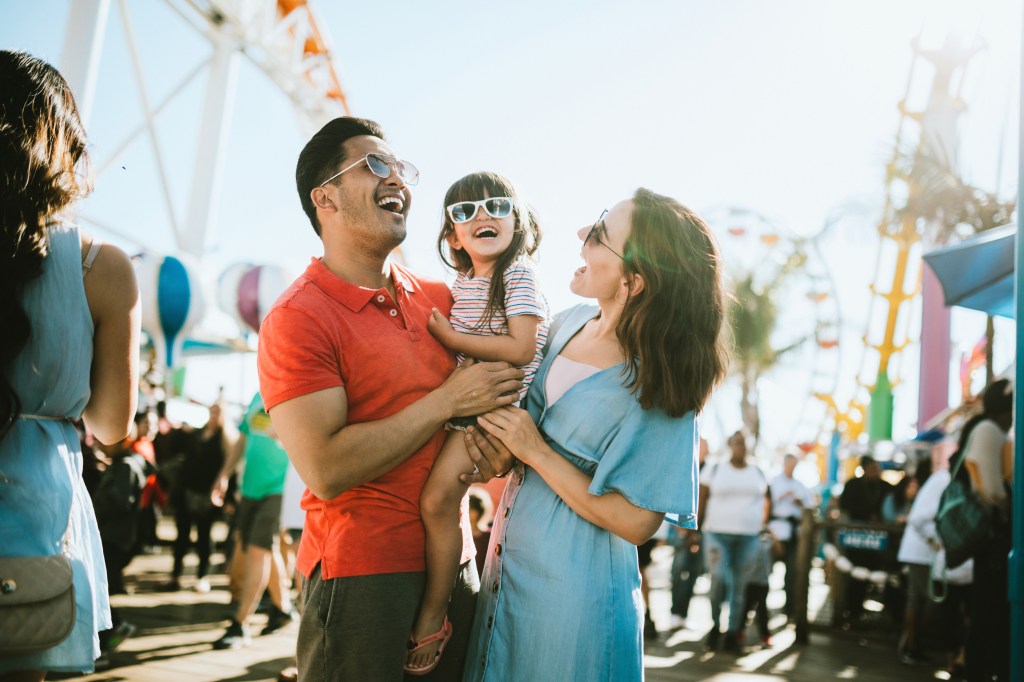 A cute mixed race family enjoys the rides and sun at the fair activities on Santa Monica Pier in Los Angeles, California. They all wear sunglasses with big smiles.