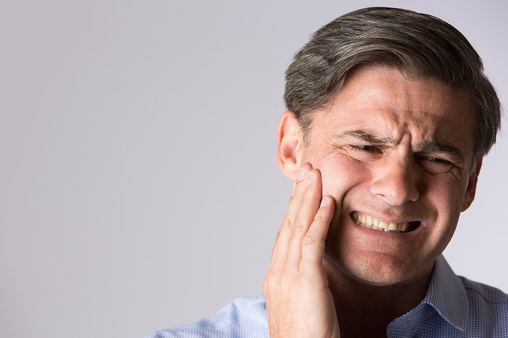 Man rubbing jaw while wincing in pain