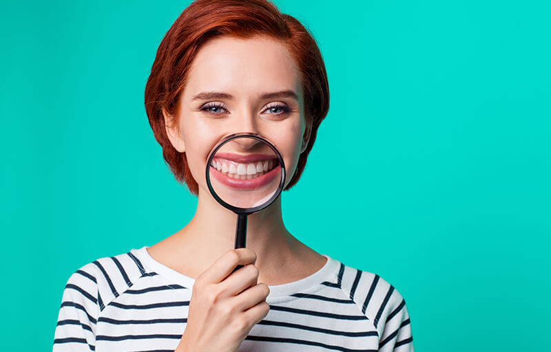 Woman holding magnifying glass up to smiling mouth