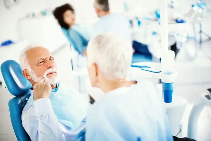 old man with pointing at mouth in dentists chair