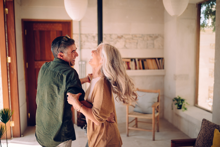 Playful mature husband and wife having fun, celebrating, dancing and laughing together in living room