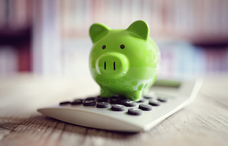 A green colored piggy bank rests upon a small calculator
