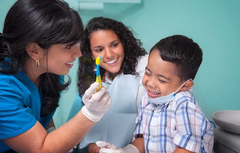 A child giggling at a toothbrush held by a dentist