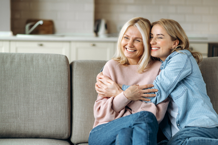 Portrait of mother and daughter. Mature attractive mother and her young adult happy daughter, are sitting at home on the couch, embracing, smiling. Family values