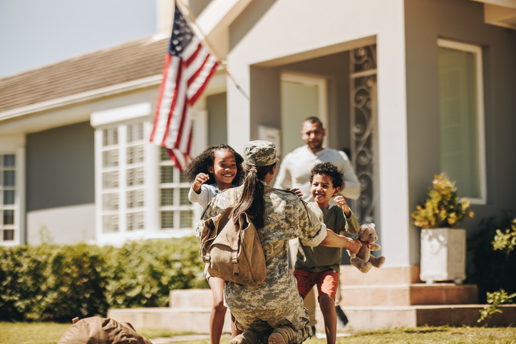 Servicewoman embracing her children after arriving home from the army. American soldier receiving a warm welcome from her husband and kids. Military woman reuniting with her family.