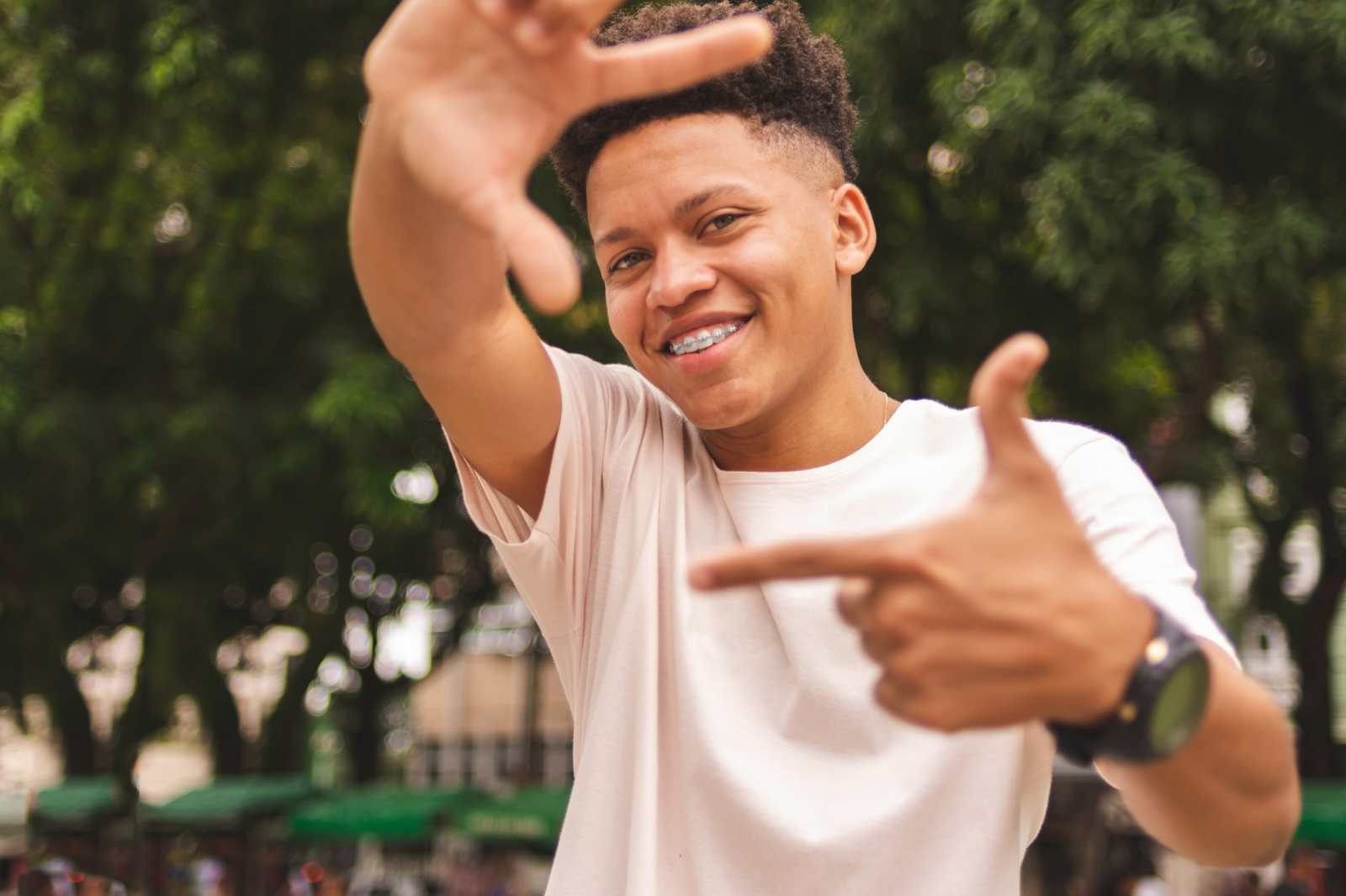 Portrait of a young man wearing braces doing frame with fingers looking at you
