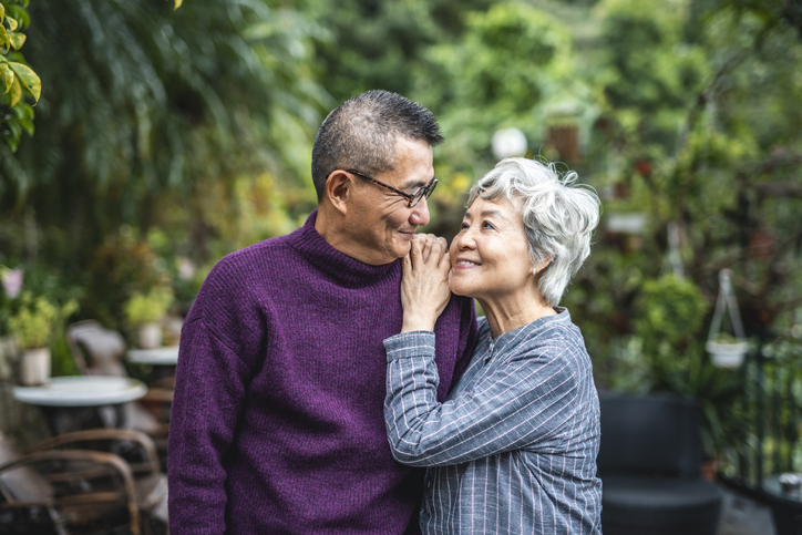 Close-up of smiling senior Chinese woman standing face to face with her contented bespectacled husband.