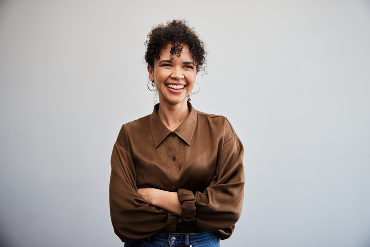 Portrait of a young businesswoman smiling while standing with her arms crossed in front of a white wall in an office