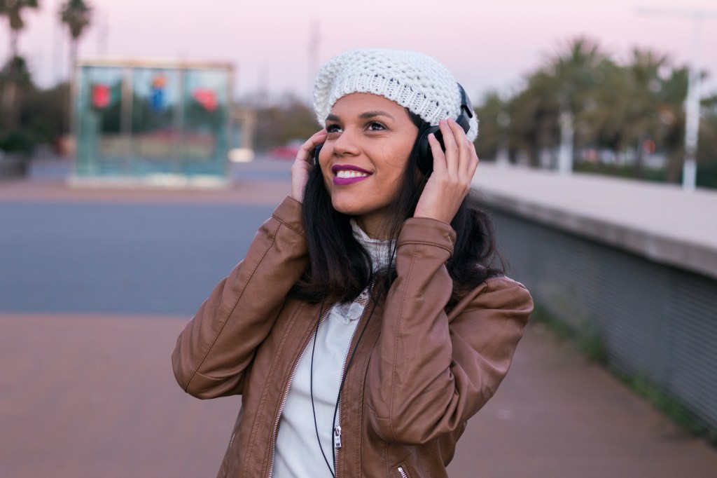Happy latin girl listening to music with headphones and a mobile phone in the street in winter