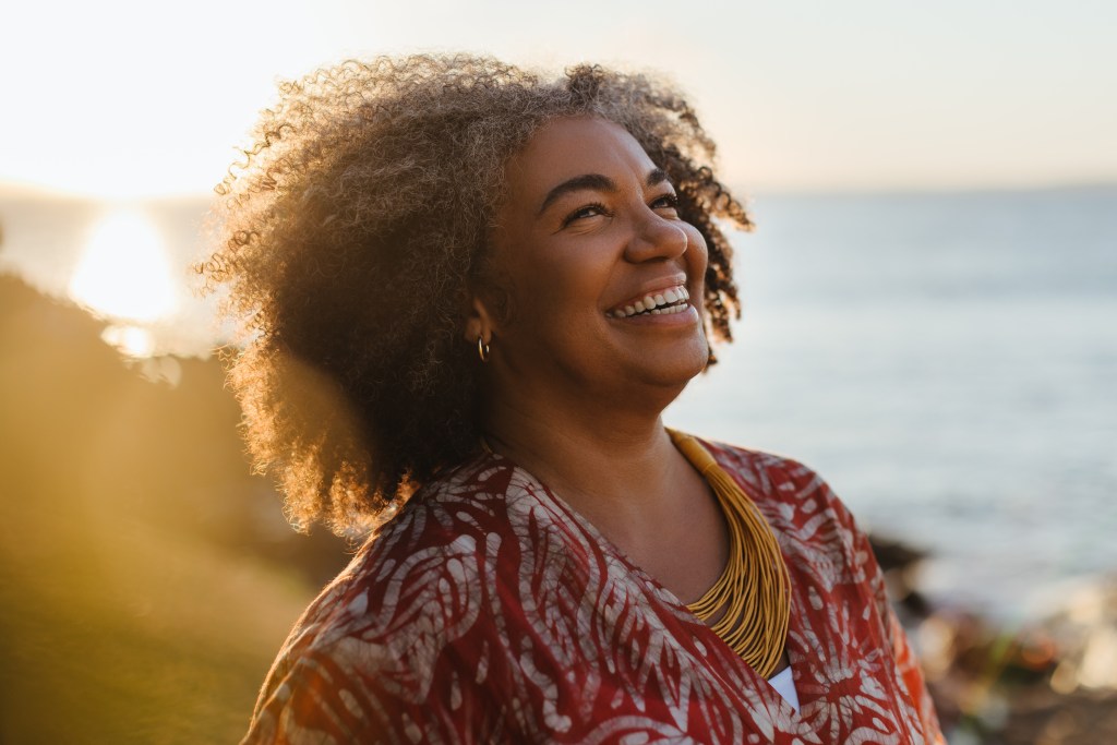 Smiling mature woman enjoying a moment of healthy living by the sea at sunset, radiating happiness and contentment.