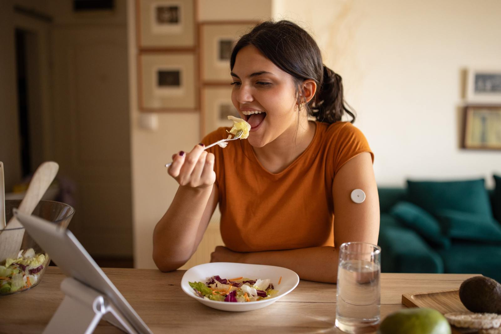Young diabetic patient teenage woman eating a healthy salad at home, she has a glucose monitor on her arm.