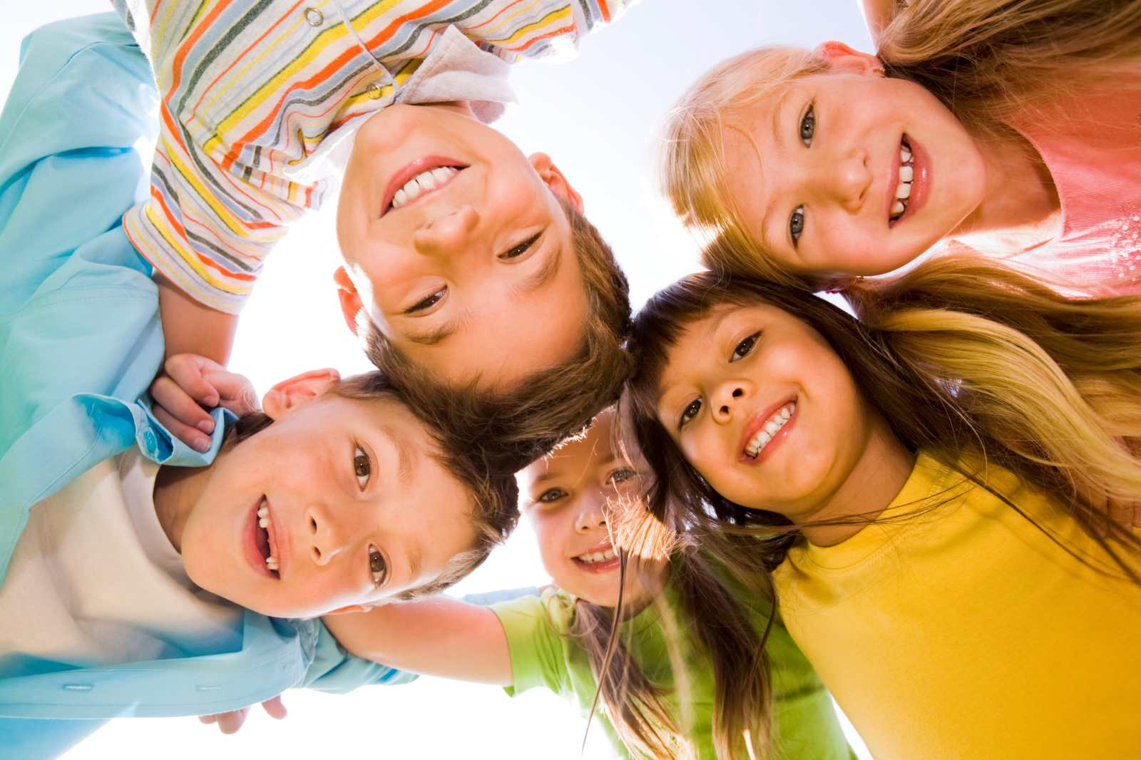 Below view of happy children embracing each other and smiling at camera