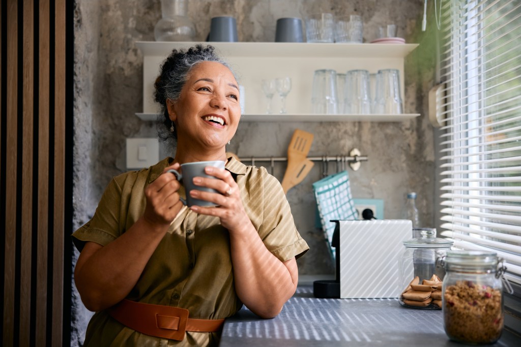 Happy mature woman drinking coffee in kitchen and looking away