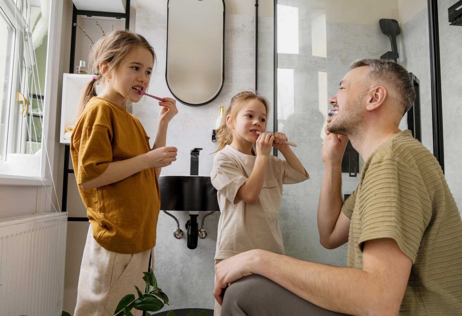 Dad teaching his young daughters how to brush their teeth