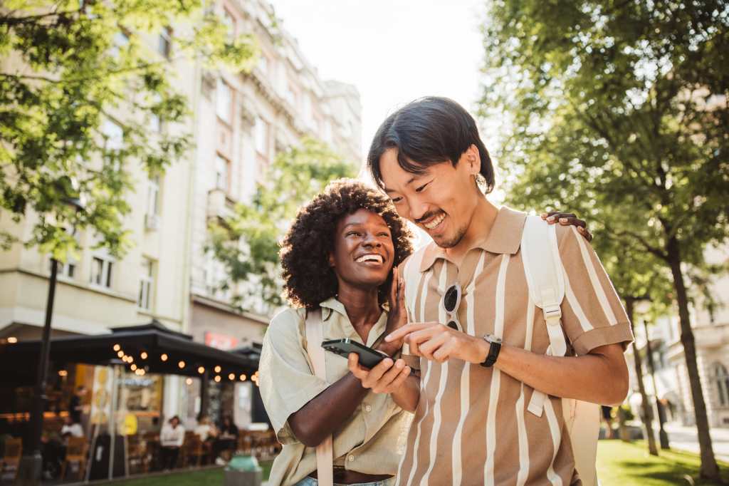 happy interracial couple talking and laughing while viewing phone