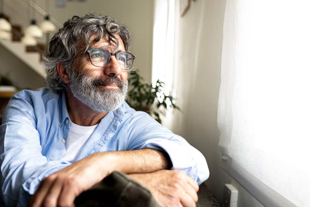 Senior man with glasses, sitting, looking out the window