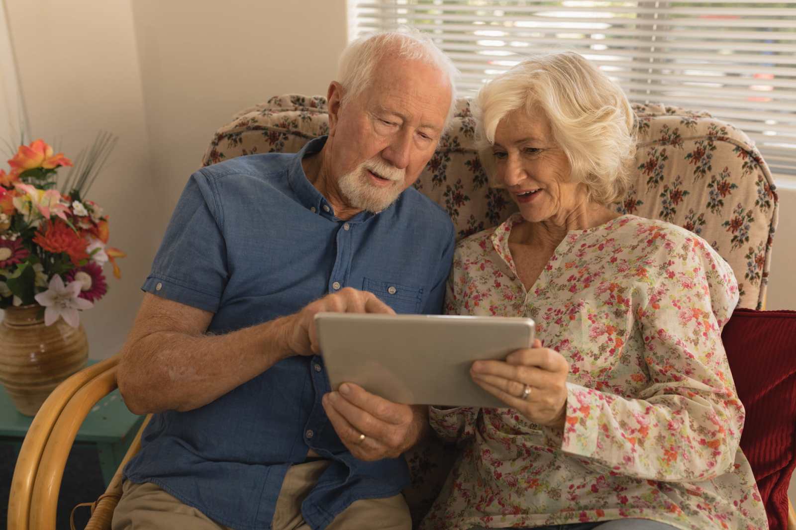 Front view of happy senior couple using digital tablet in living room at nursing home
