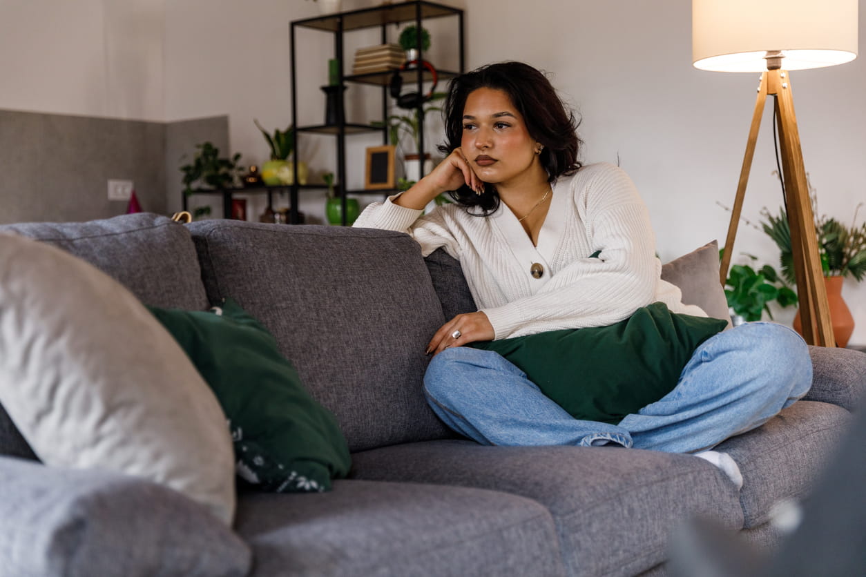 Young woman sitting on the couch deep in thought