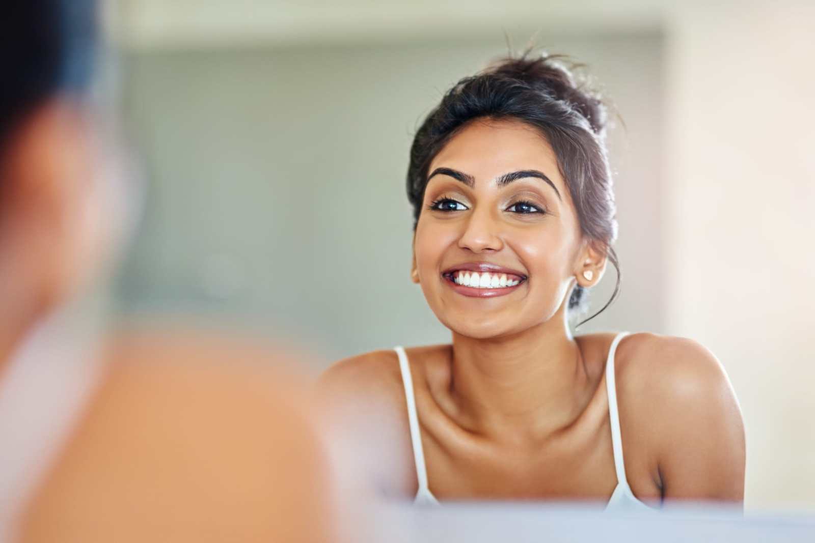 Cropped of a young woman looking at her straight smile in the bathroom mirror